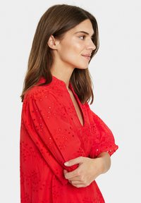 Red, embroidered dress with a loose fit, v-neck, and puff sleeves. Features floral patterns and eyelet cutouts for added detail.