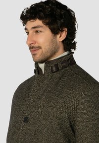 Brauner Wollmantel mit strukturiertem Hahnentrittmuster, Lederakzenten am Kragen, Ein-Knopf-Verschluss und hohem Stehkragen.