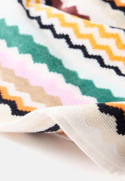 Tissu doux avec des rayures zigzag multicolores en orange, noir, vert, beige et rose sur fond blanc, plié au bord.
