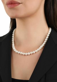 Collar de perlas con perlas redondas, blancas y brillantes, distribuidas de manera uniforme, usado sobre una chaqueta negra. Diseño simple sin adornos adicionales.