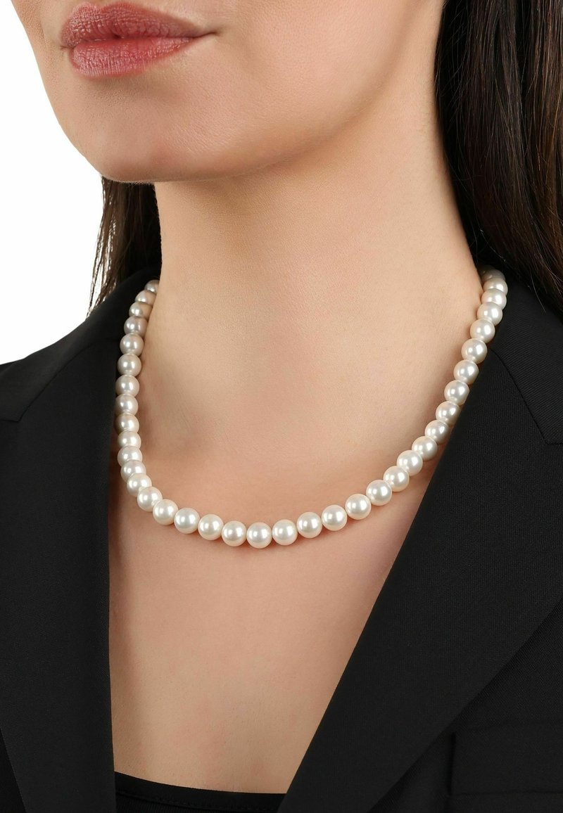 Collar de perlas con perlas redondas, blancas y brillantes, distribuidas de manera uniforme, usado sobre una chaqueta negra. Diseño simple sin adornos adicionales.