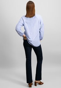 Camicia a maniche lunghe di colore azzurro chiaro con maniche arricciate, abbinata a jeans svasati in denim scuro e sandali con tacco a blocco marroni.