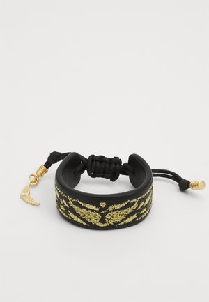 Brățară din piele neagră cu un model decorativ aurit, având un șnur ajustabil negru și un mic pandantiv în formă de aripă aurie.