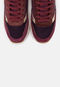 Lila och vinröda sportskor har en kombination av mesh och texturerat mockamaterial, med snörning och en dämpad sula.