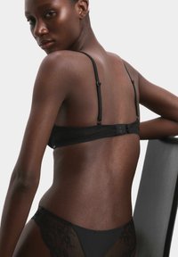 Reggiseno in pizzo nero con spalline regolabili e chiusura a gancio, che mostra dettagli in pizzo intricati e una finitura liscia e opaca.