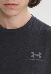 Mörkgrå bomullst-shirt med rundhals och korta ärmar, med en ljusgrå "Under Armour"-logotyp på vänster bröst.