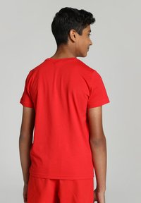 Červené bavlnené tričko s krátkymi rukávmi, okrúhlym výstrihom a voľným strihom, zobrazené zozadu. Hladká textúra bez vzorov.