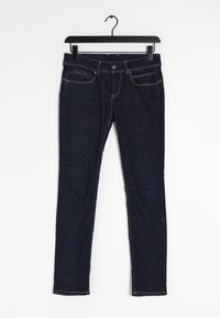 Mörkblå denimjeans hängande på en svart galge. De har framfickor, dragkedja och kontrasterande sömmar längs både kanterna.
