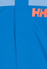 Chaqueta deportiva azul con una franja horizontal de color azul claro, que presenta un prominente logo naranja "HH". Textura suave, costuras reforzadas y diseño práctico.