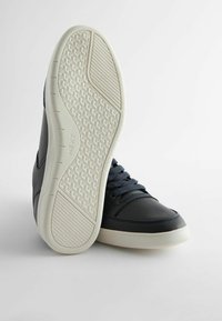 Sneaker in pelle blu navy con accenti texturizzati e punta tondeggiante. La suola in gomma bianca presenta una grip a motivo. I lacci scuri completano il design.