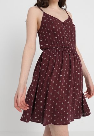 Robe sans manches bourgogne avec une taille cintrée, présentant un tissu à motifs avec de petites accents blancs et une jupe évasée.
