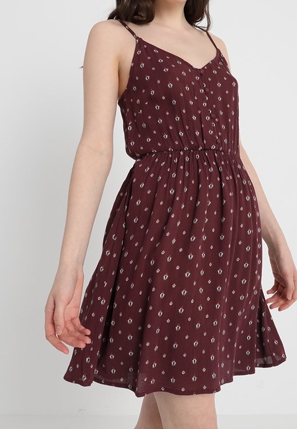 Robe sans manches bourgogne avec une taille cintrée, présentant un tissu à motifs avec de petites accents blancs et une jupe évasée.