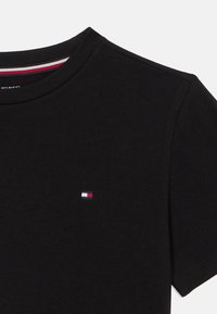 Μαύρο κοντομάνικο μπλουζάκι με στρογγυλή λαιμόκοψη και μικρό ορθογώνιο λογότυπο σε κόκκινο, άσπρο και μπλε στην αριστερή πλευρά του στήθους.