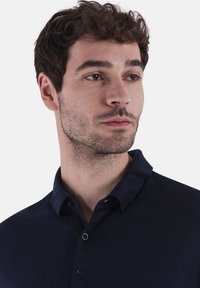 Polo shirt blu navy in tessuto texturizzato, con colletto classico e tre bottoni. Design aderente che enfatizza la scollatura e le spalle.