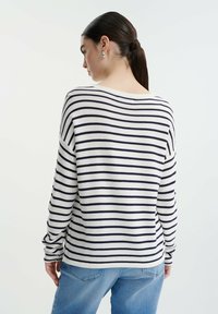 Gestreepte trui in wit en marineblauw, met een relaxte pasvorm, brede halslijn en lange mouwen. G draagt met lichtblauwe jeans.