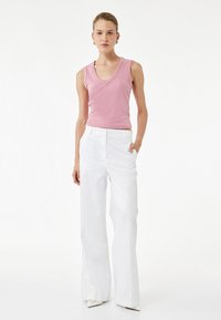 Top rosa sin mangas con escote en V, combinado con pantalones blancos de cintura alta. Textura suave y ajuste a medida, complementado con zapatos blancos de punta.