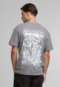 Gray cotton t-shirt featuring a graphic print on the back with a skull, flames, and a cityscape, along with text details.