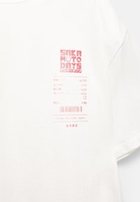 Witte katoenen t-shirt met een ontwerp in rode tekst met "SAKA MOTOR DAYS" en verschillende kanji-tekens, samen met een streepjescode en speelse berichten.