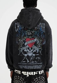 Black, oversized hoodie with a graphic design featuring a heart, skull, and floral elements on the back. Made of soft, textured fabric.