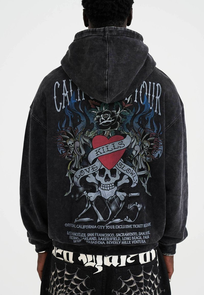 Black, oversized hoodie with a graphic design featuring a heart, skull, and floral elements on the back. Made of soft, textured fabric.