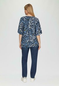 Blauw luipaardprint top met een losse pasvorm en korte mouwen, gecombineerd met donkerdenim jeans en zilveren sneakers. Gelaagd materiaal met een ontspannen silhouet.