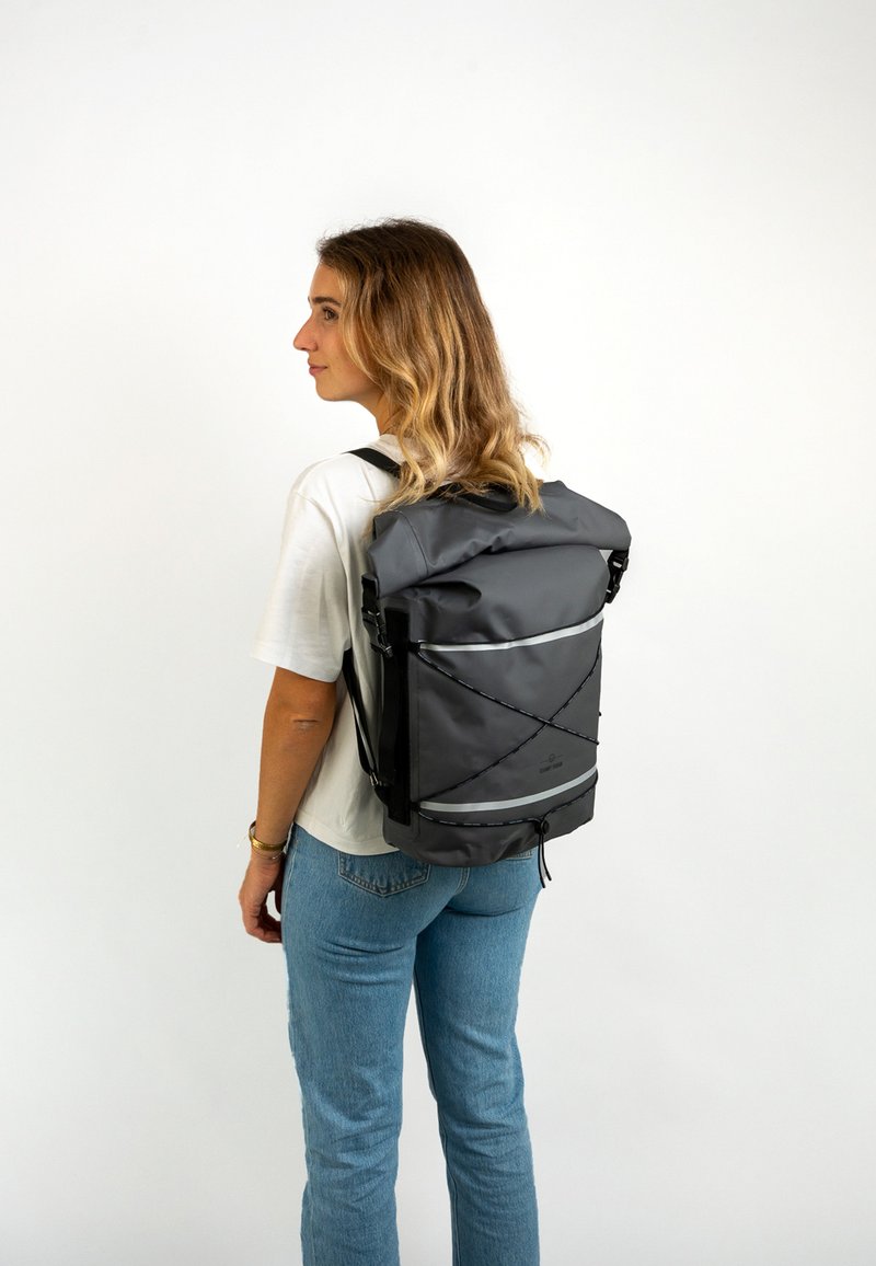 Mochila gris tipo roll-top con correas ajustables, acentos reflectantes y cordón bungee en el frente, fabricada con material duradero y resistente al agua.