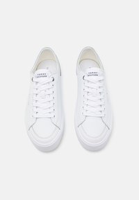 Zapatillas blancas con parte superior de cuero suave, punta redondeada y suelas de goma planas. Presenta un sistema de cordones en la parte delantera y un sutil logotipo en la lengüeta.