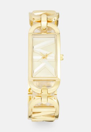 Reloj de pulsera en tono dorado con una esfera rectangular, correa texturizada clara y manecillas que indican la hora en el centro. Presenta patrones geométricos.