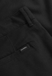 Tissu noir texturé des pantalon avec des coutures visibles et une étiquette GABBA sur la taille. Le matériau semble durable et côtelé.