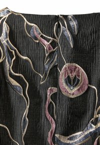 Artimas juodo audinio tekstūros vaizdas su abstrakčia gėlių siuvinėjimu metaliniais aukso, mėlynos ir violetinės spalvos tonais, kuriame yra centrinis juodas užtrauktukas.