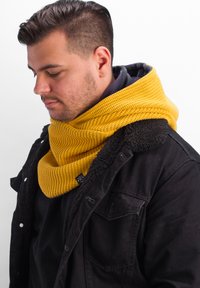 Knit yellow cowl scarf featuring a ribbed texture, worn over a dark jacket with a fleece collar, enhancing warmth and coverage.