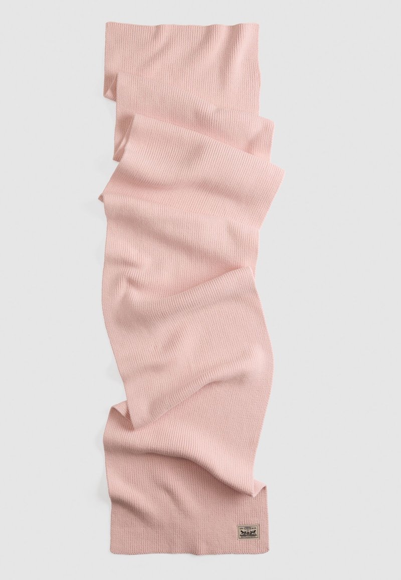 Écharpe tricotée rose douce avec une texture côtelée, étalée à plat et légèrement pliée, avec une petite étiquette rectangulaire en tissu à une extrémité.