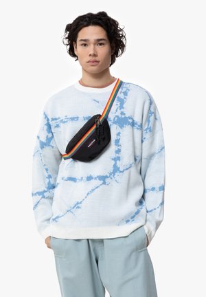 Světle modrý svetr s bílým tie-dye vzorem, kombinovaný s černou kabelkou přes rameno s vícebarevným pruhovaným popruhem.