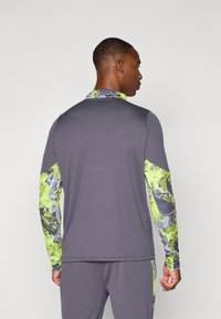 Long-sleeve athletic shirt in gray with green and gray patterned accents on the sleeves. Textured fabric, fitted design, and high collar.