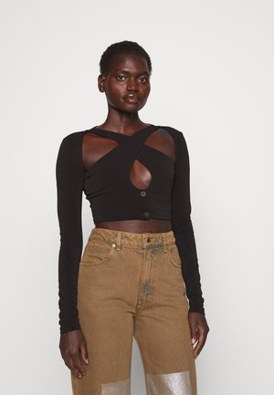 Top noir à manches longues, cropped, avec un design à découpes et une fermeture à boutons, associé à un jean en denim marron taille haute avec des accents métalliques.