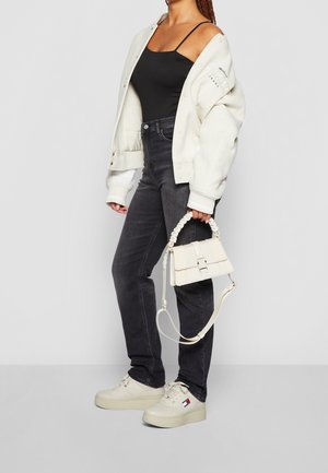 Biała, oversize'owa kurtka, czarny top na ramiączkach, ciemne dżinsy, kremowe sneakersy z logo oraz mała kremowa torebka z plecionym uchwytem.