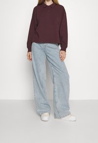 Vínová polokošile s dlouhým rukávem a třemi knoflíky, doplněná světle modrými džínami širokých nohavic. Neformální outfit dokončují bílé tenisky.