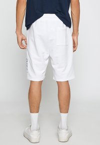 Pantalones cortos de algodón blancos con un corte relajado, que cuentan con una cinturilla elástica, bolsillo lateral y detalle de logo en la pierna izquierda.