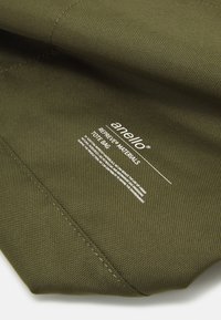 Sac fourre-tout vert olive fabriqué à partir de matériaux REPREVE®. Comprend un tissu texturé et une étiquette imprimée avec les instructions d'entretien et le nom de la marque.