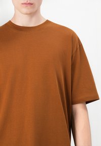 Brun bomulds t-shirt med rund halsudskæring og korte ærmer. Stoffet ser blødt ud med en glat struktur og minimale sømme.