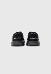 Black athletic shoes with a sleek design, featuring a textured upper and transparent midsole. "HUGO" logo prominently displayed on the heel.