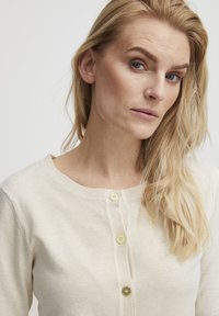 Creme cardigan med rund halsudskæring, ribbet struktur og fem guldtonede knapper langs fronten til lukning.