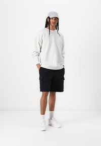 Lysegrå sweatshirt med løs pasform, sorte cargo shorts, hvide sneakers og en grå kasket. Glat tekstur og praktiske designfunktioner.