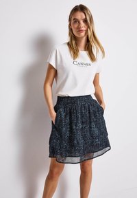 Weißes T-Shirt mit dem Aufdruck "Cannes"; geschichteter schwarzer Rock mit strukturiertem Muster; elastischer Bund; Taschen auf jeder Seite.