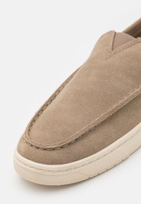 Pantofii slip-on din suede bej, cu vârful rotunjit, caracterizat prin accente de cusătură și o talpă din cauciuc texturat. Căptușeală interioară netedă.