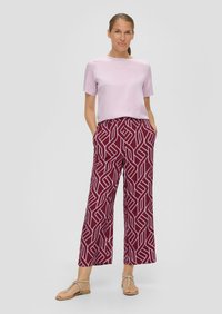 Lichtpaarse top met korte mouwen, gecombineerd met brede bordeauxrode broek met een geometrisch wit patroon. Het model draagt eenvoudige sandalen.