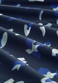 Textil mit einem dunklen Marinehintergrund und abstrakten blauen und hellgrünen Formen. Glatte Textur mit einem subtilen Glanz und gefalteten Schichten.