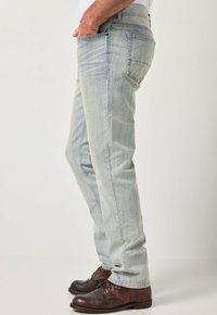 Vaqueros de mezclilla azul claro con corte recto, que cuentan con cinco bolsillos y un desvanecimiento sutil. Combinados con zapatos marrón oscuro con cordones.