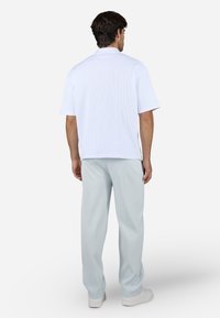 Polo bianco a maniche corte con texture a costine, abbinato a pantaloni larghi azzurri, mostrato di schiena, su uno sfondo neutro.