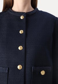 Navy textured jacket featuring a crew neck, gold lion-embossed buttons, and dual front pockets with braided accents.